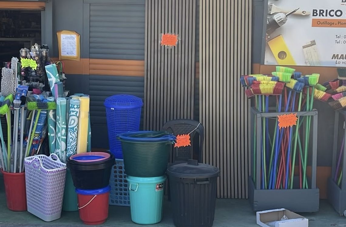 Rayon solderie et bazar devant le magasin : balais, bassines, poubelles et articles à petits prix